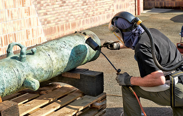 Application à chaud d’une patine protectrice sur un canon de bronze pour le musée de la Marine de Brest.