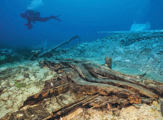 Photo sous l'eau de l'épave du sanguinaire C, avec un plongeur amenant une des ancres de l'épave à la main.