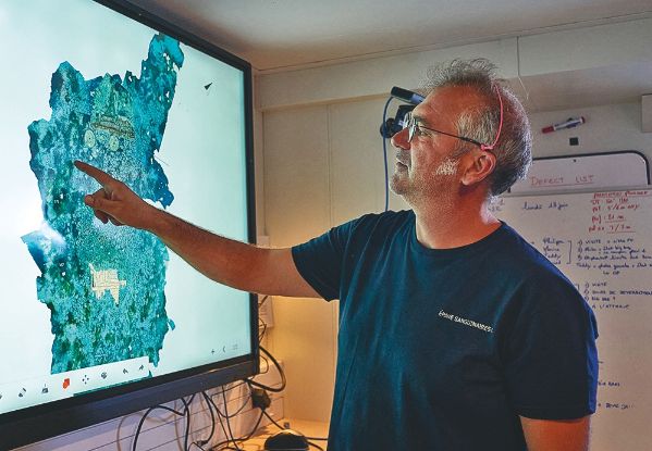 Membre de l'équipage pointant le plan de l'épave devant une télé.