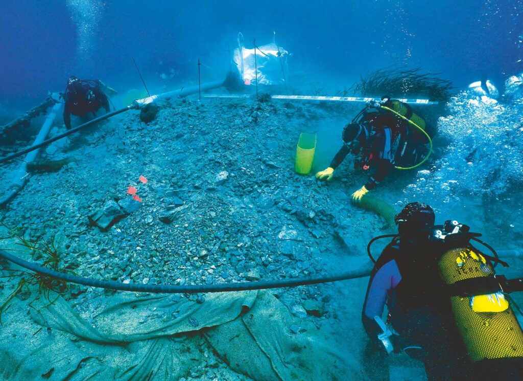 3 plongeurs, sous l'eau, déplaçant les roches au dessus d'un vestige.