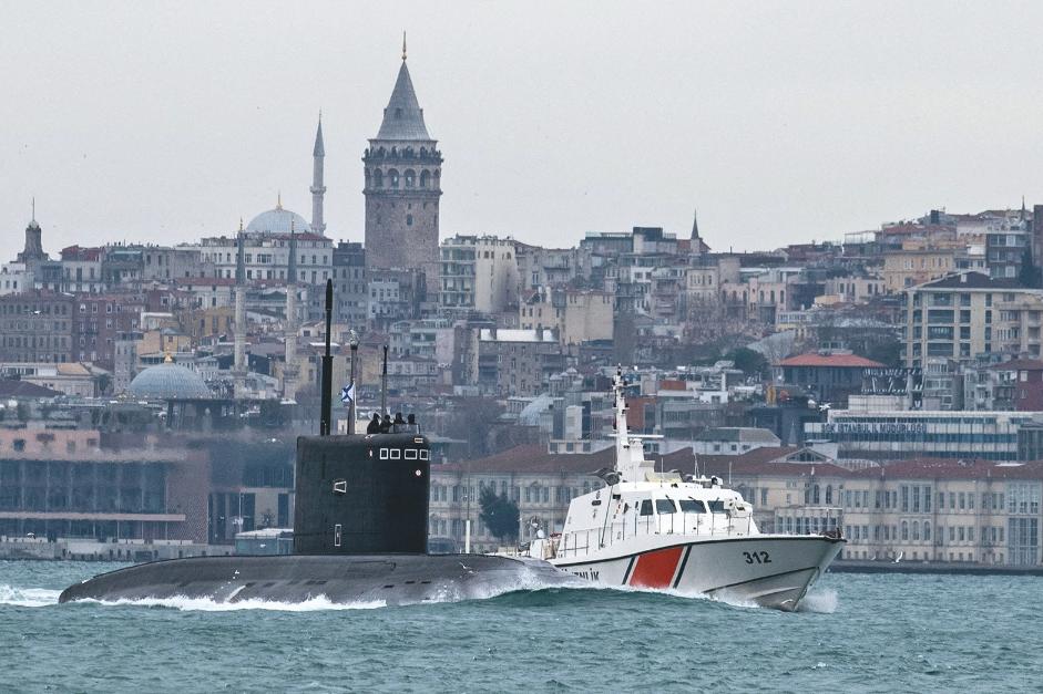 Proche d'une ville, un sous-marin, légèrement hors de l'au, accompagné par un bateau garde-côte.