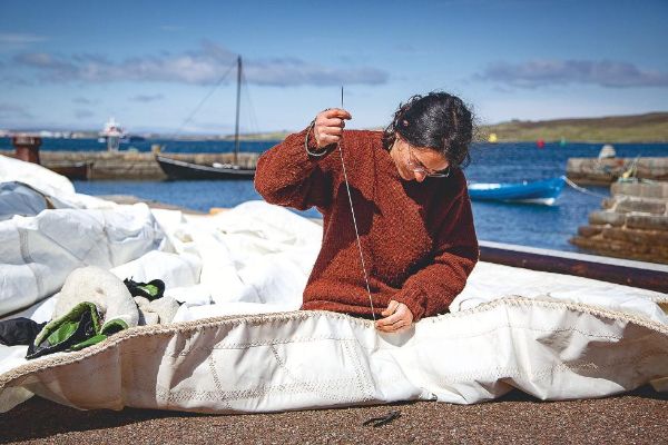 Membre de l'équipe cousant la voile du bateau.